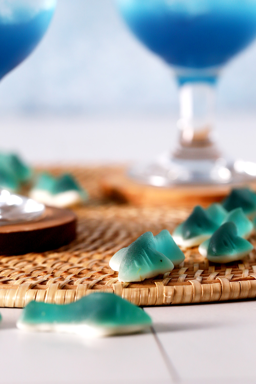 Gummy sharks lying on a placemat underneath blue mocktails.