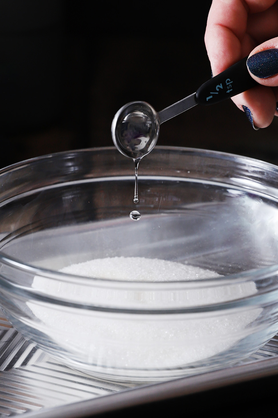 Peppermint extract getting poured into white sugar in a bowl.