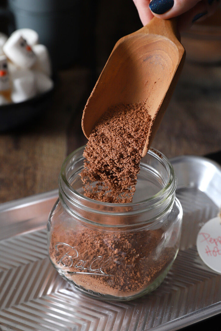 Finished peppermint hot cocoa mix being poured from a wooden scoop into a mason jar.