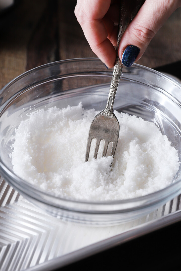 A hand using a fork to combine white sugar and peppermint extract.