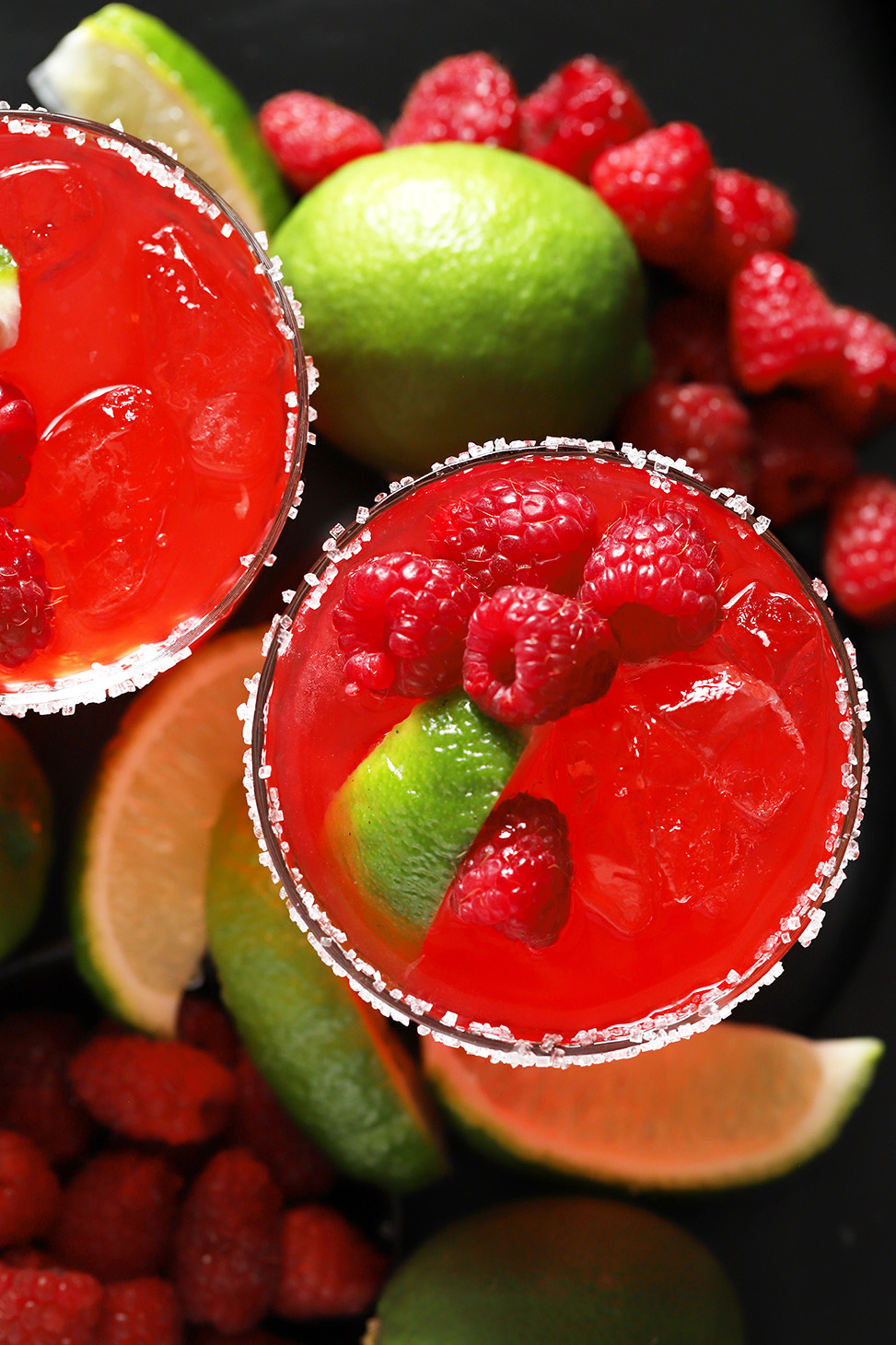 Looking down at 2 glasses of raspberry margaritas garnished with fresh raspberries, lime slices and salt rims.