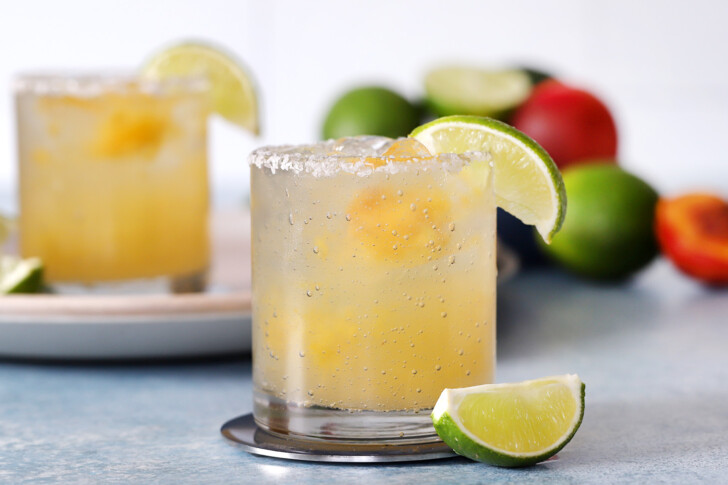 A glass of peach margarita garnished with a lime wedge.