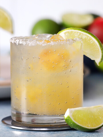 A glass of peach margarita garnished with a lime wedge.