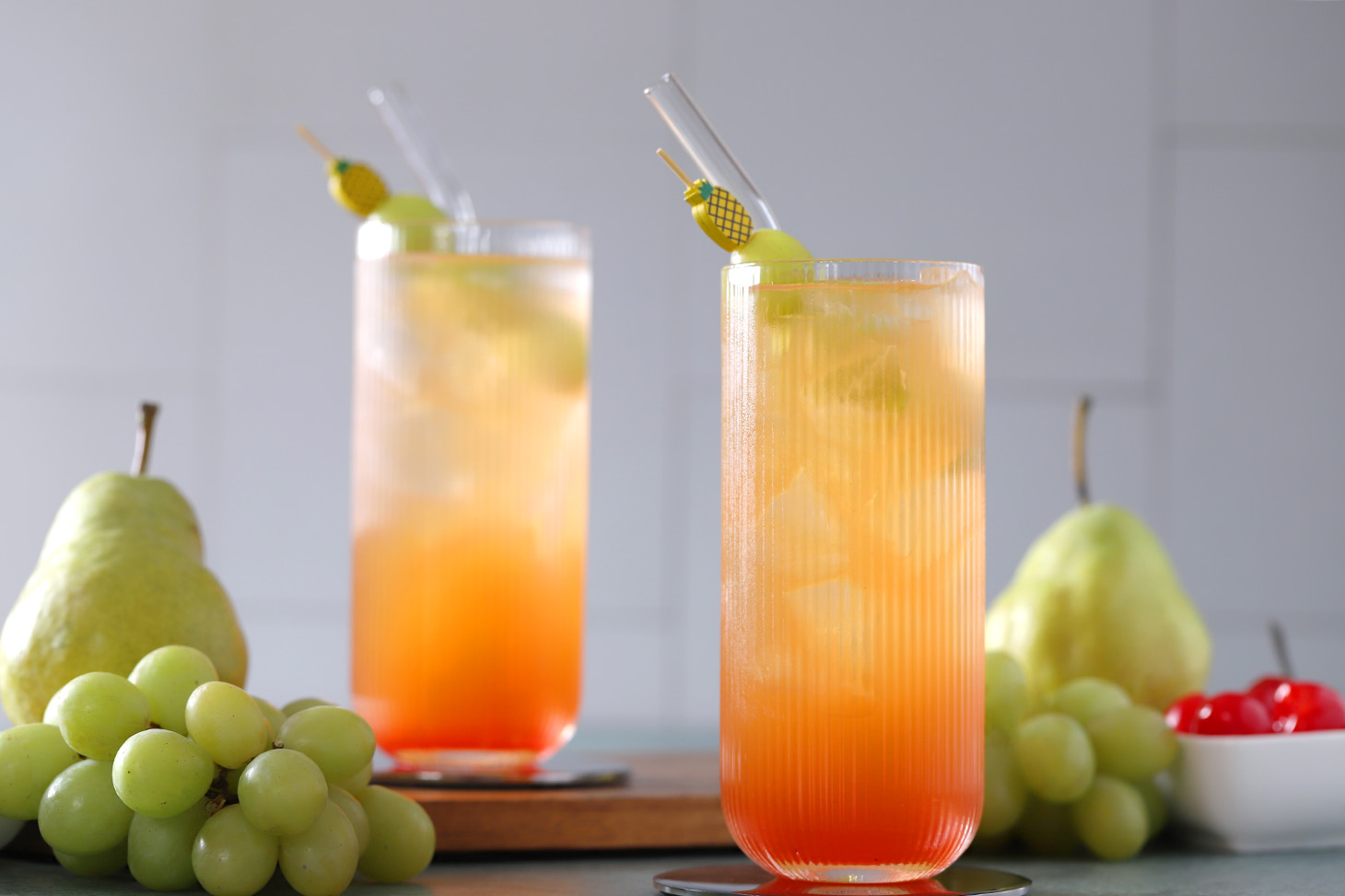 Glasses of fruit punch mocktail garnished with green grapes on pineapple cocktail picks.