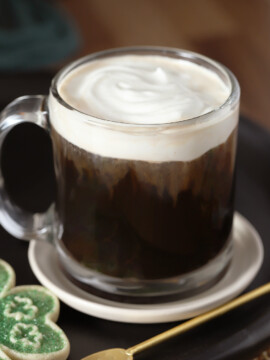 A glass mug of Irish coffee topped with whipped cream.