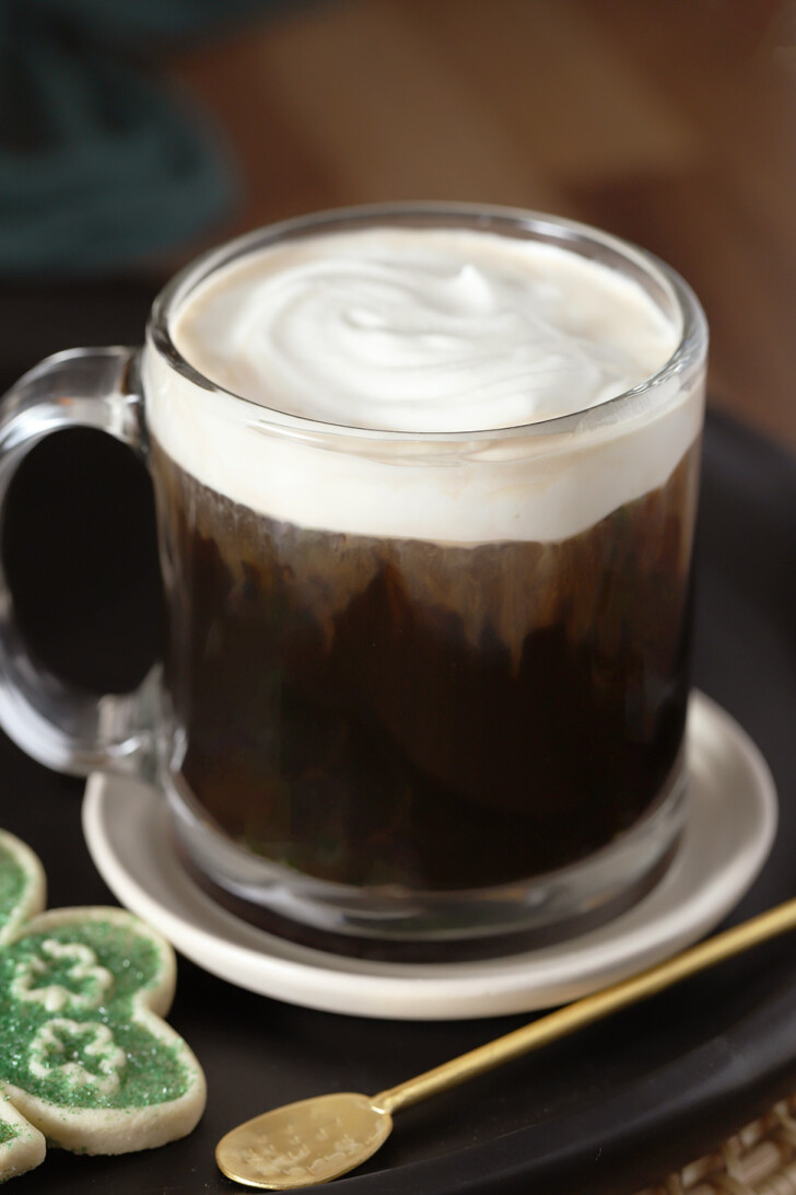 A glass mug of Irish coffee topped with whipped cream.