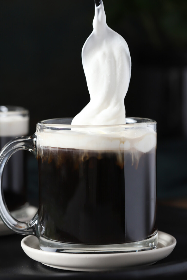 A spoon gently placing whipped heavy cream onto the top of the coffee.