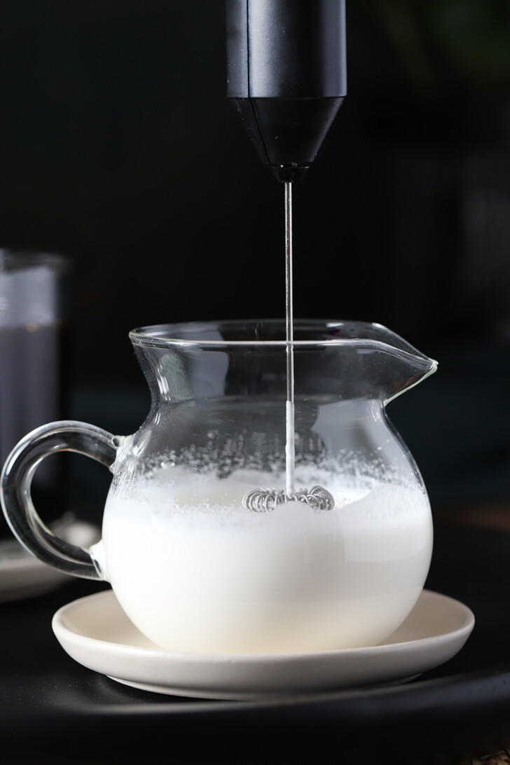 A milk frother in a glass jar of cream.