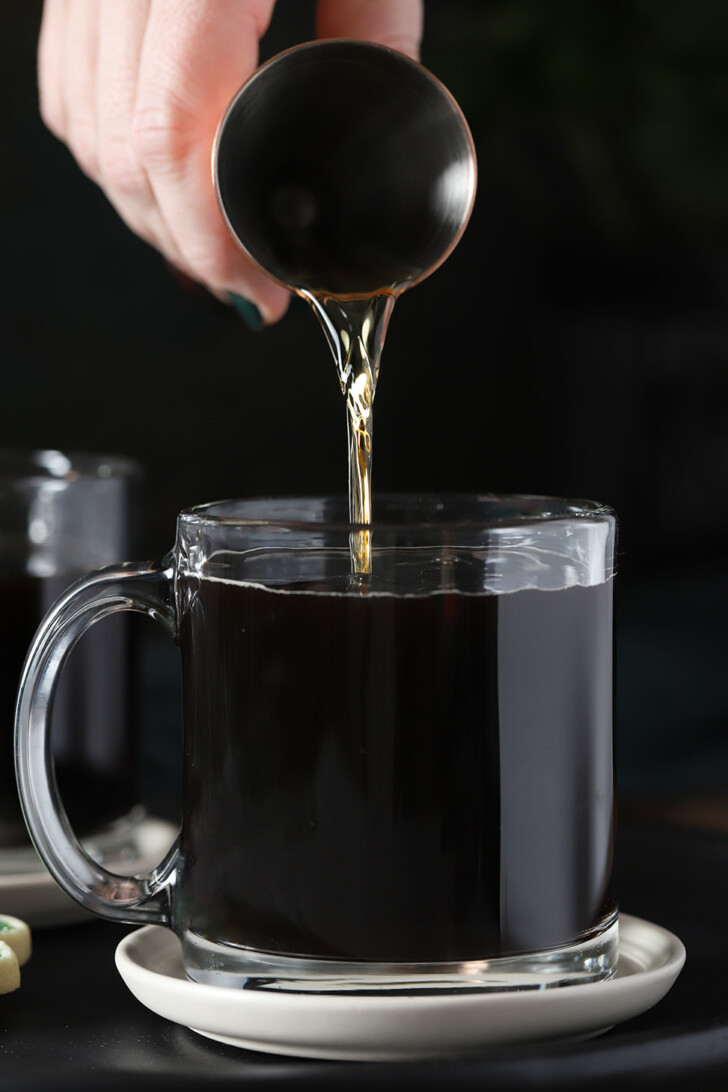 A hand pouring Irish whiskey into a glass mug of coffee.