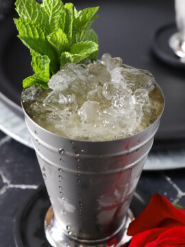 A silver cup filled with crushed ice, mint julep cocktail, and a large sprig of mint.