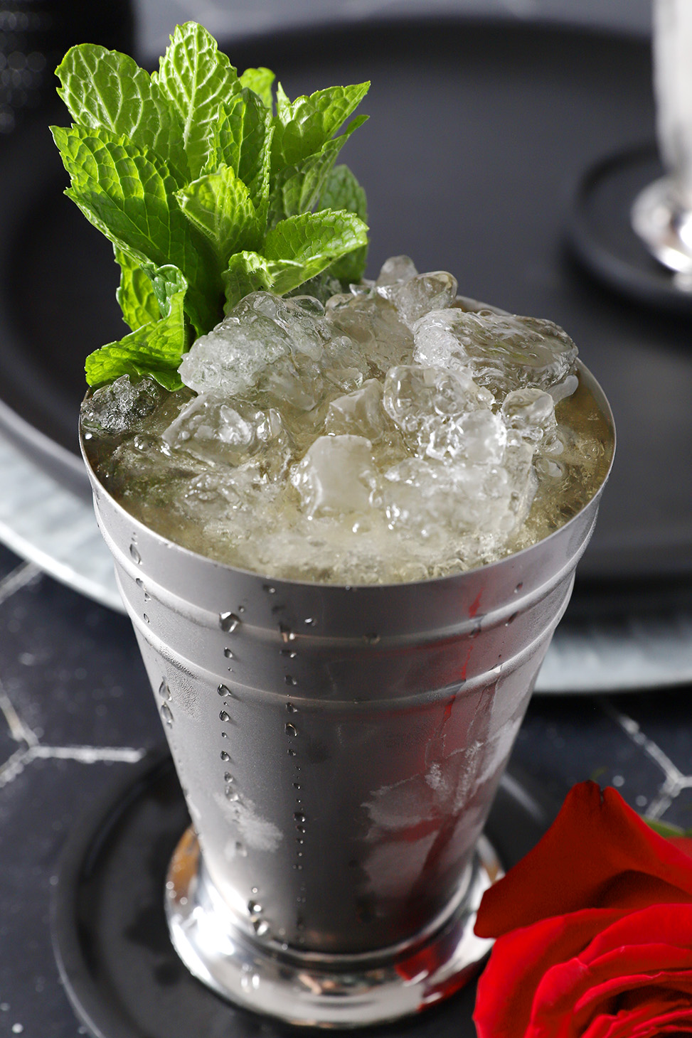 A silver cup filled with crushed ice, mint julep cocktail, and a large sprig of mint.