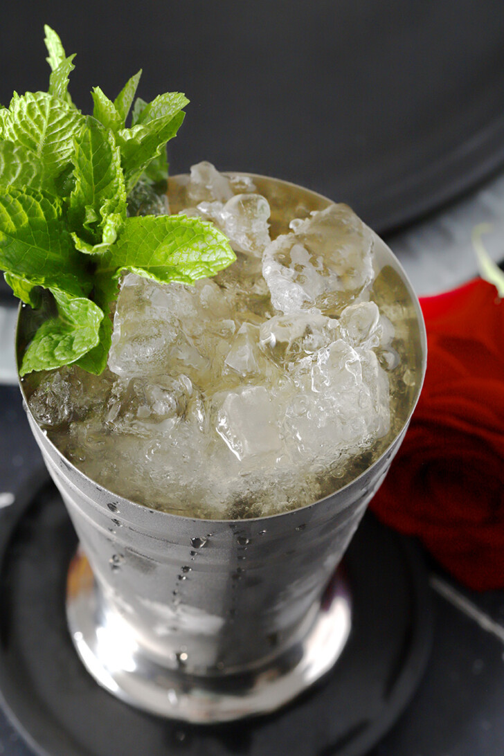 A silver cup filled with crushed ice, mint julep cocktail, and a large sprig of mint.