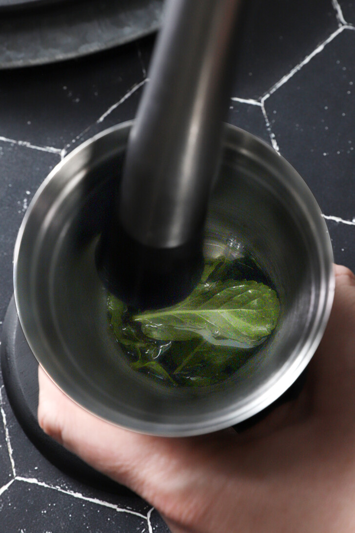 A hand holding a julep cup and muddling mint leaves.