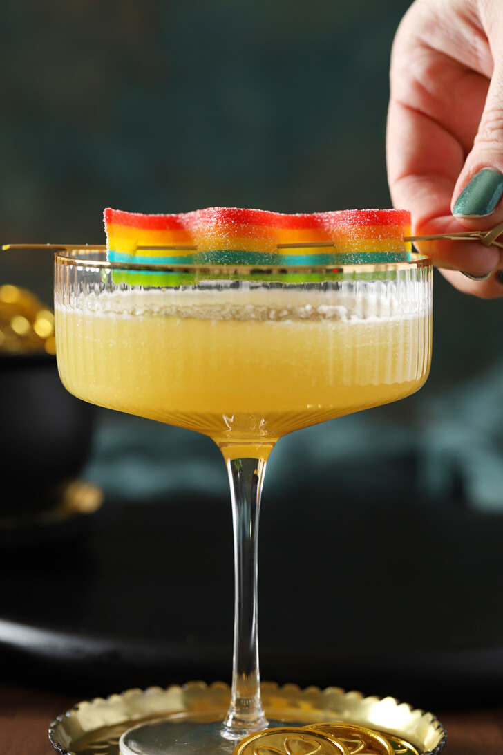 A hand setting rainbow candy garnish onto a pot of gold st paddy's day mocktail.