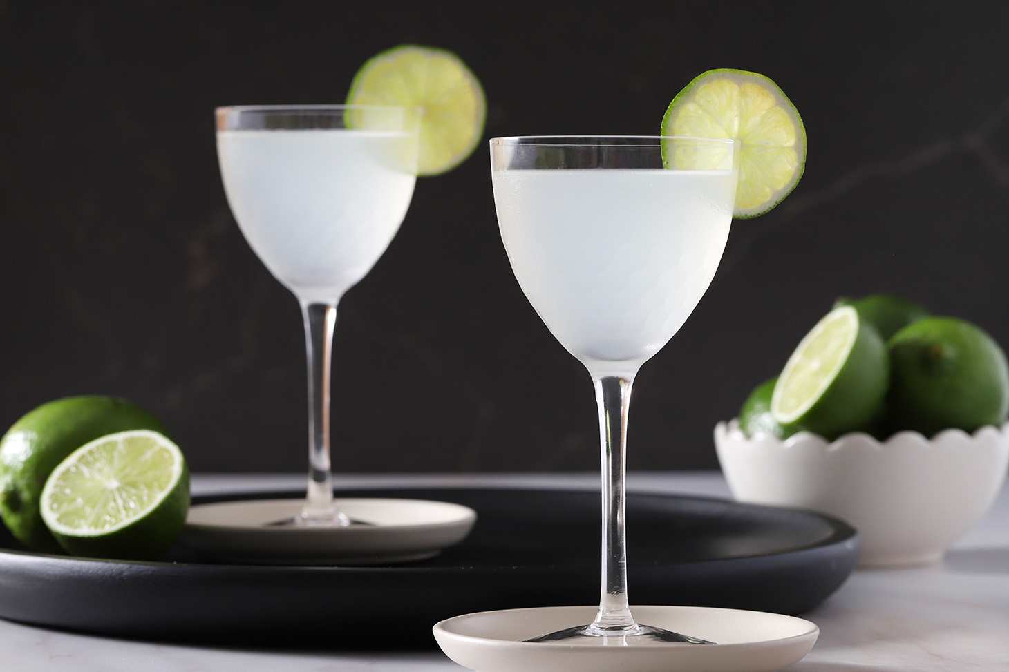 Two glasses of gin gimlets garnished with lime wheels.
