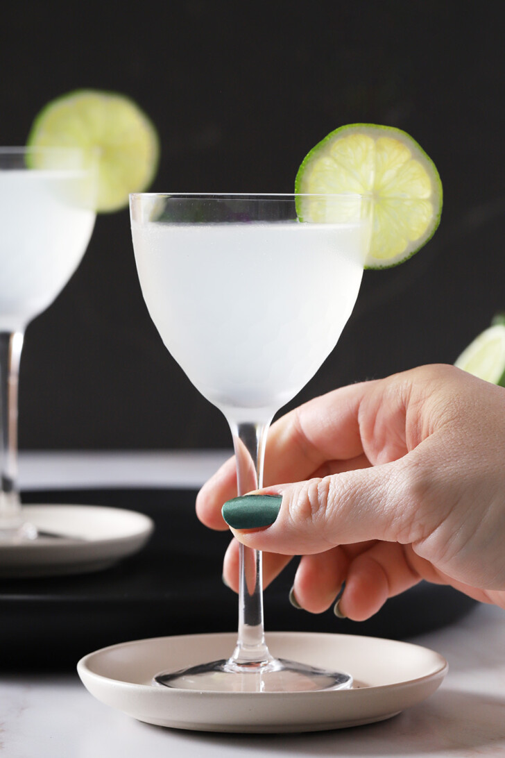 A hand reaching out to pick up a glass of gin gimlet.