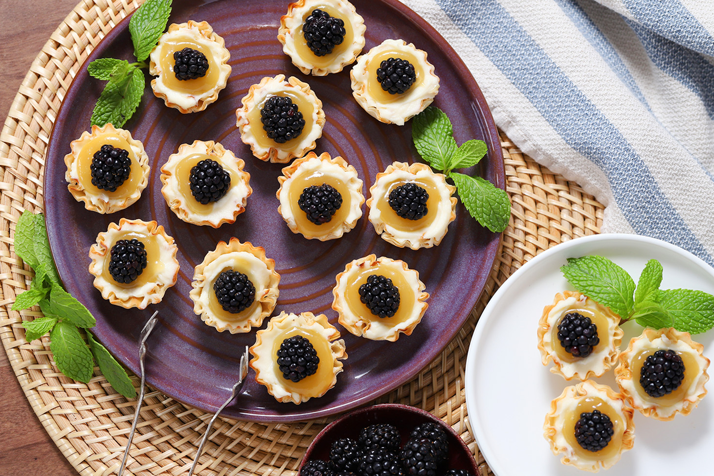 A platter full of mini lemon tarts with blackberries on them.