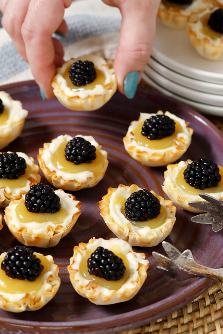 A hand taking a mini tart off of a platter filled with lemon tarts.