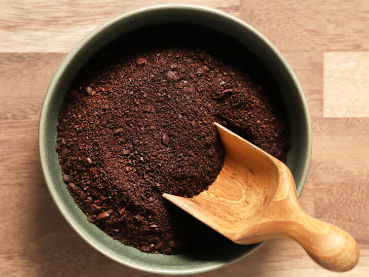 A bowl of coarse ground coffee with a wooden scoop in it.