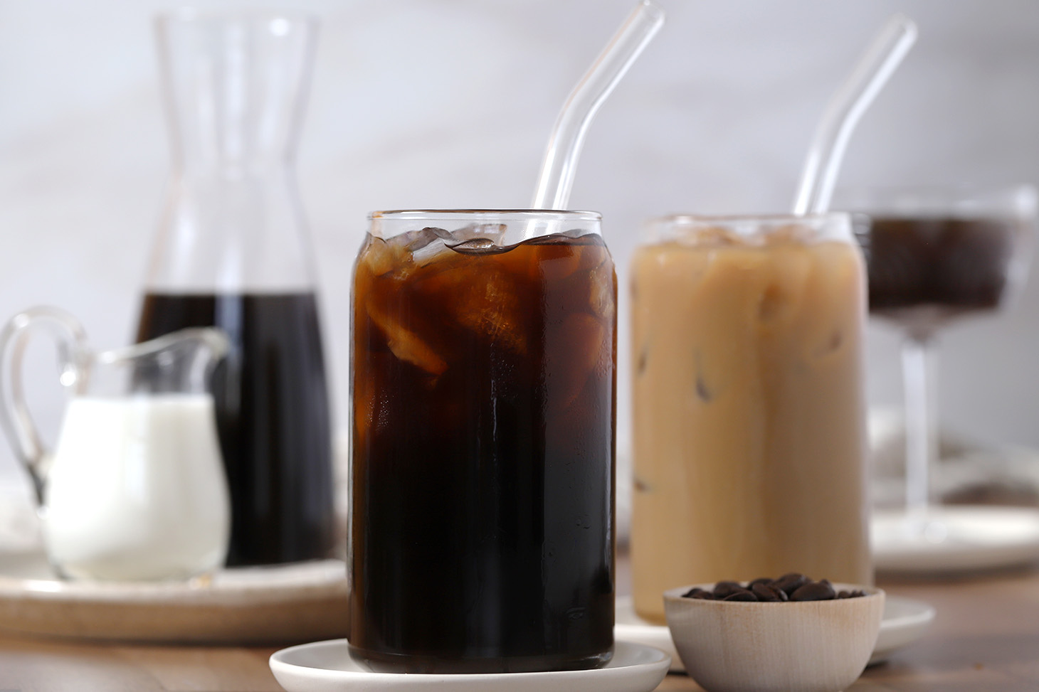 Glasses filled with various uses for espresso cold brew coffee, a pitcher of milk, and a carafe of cold brew.