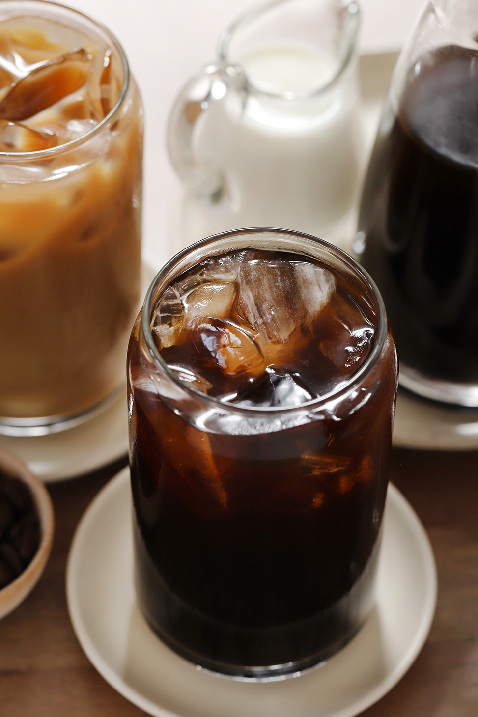 A glass filled with espresso cold brew coffee and ice, surrounded by a pitcher of milk and more cold brew coffee. 