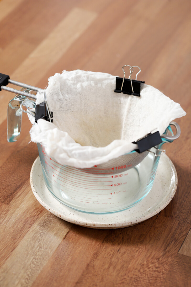 Cheese cloth placed over a strainer and clipped in place with binder clips, set over a 4 cup measuring cup.