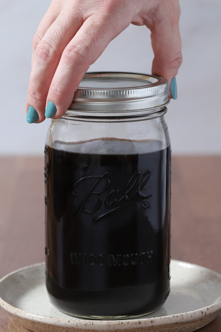 A hand screwing a lid onto a large mason jar of cold brew coffee.