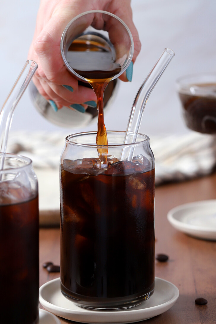 A hand pouring cold brew coffee into a glass over ice.