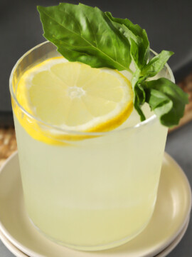 A glass of Gin Smash cocktail garnished with a lemon wheel and fresh basil leaves.