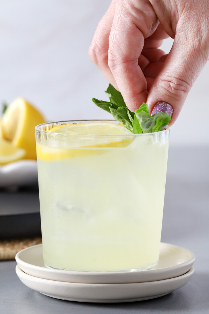 A hand placing a sprig of basil into a glass of gin smash for garnish.