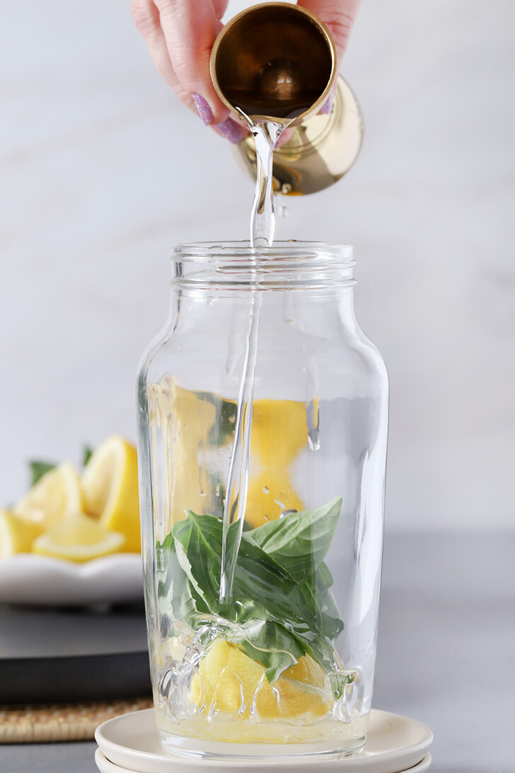 A hand pouring simple syrup into a cocktail shaker with bail and lemon in it.