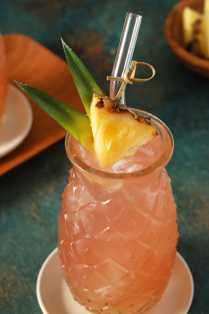 A glass of Malibu Bay Breeze garnished with a wedge of pineapple and pineapple leaves.