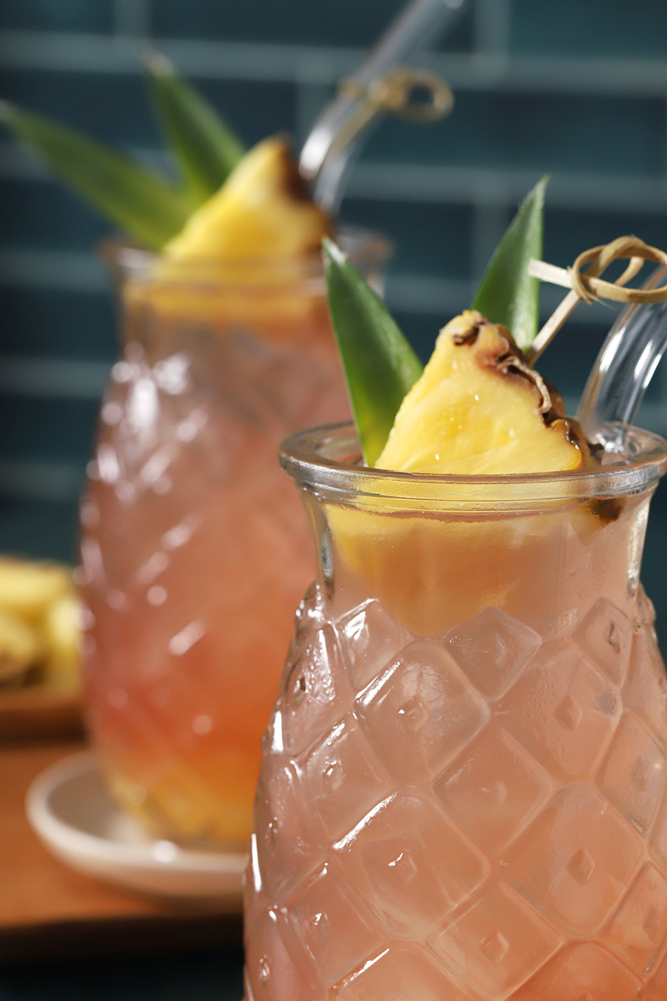 Pineapple shaped glasses of Malibu Bay Breeze cocktail garnished with wedges of pineapples and pineapple leaves in a cocktail pick.