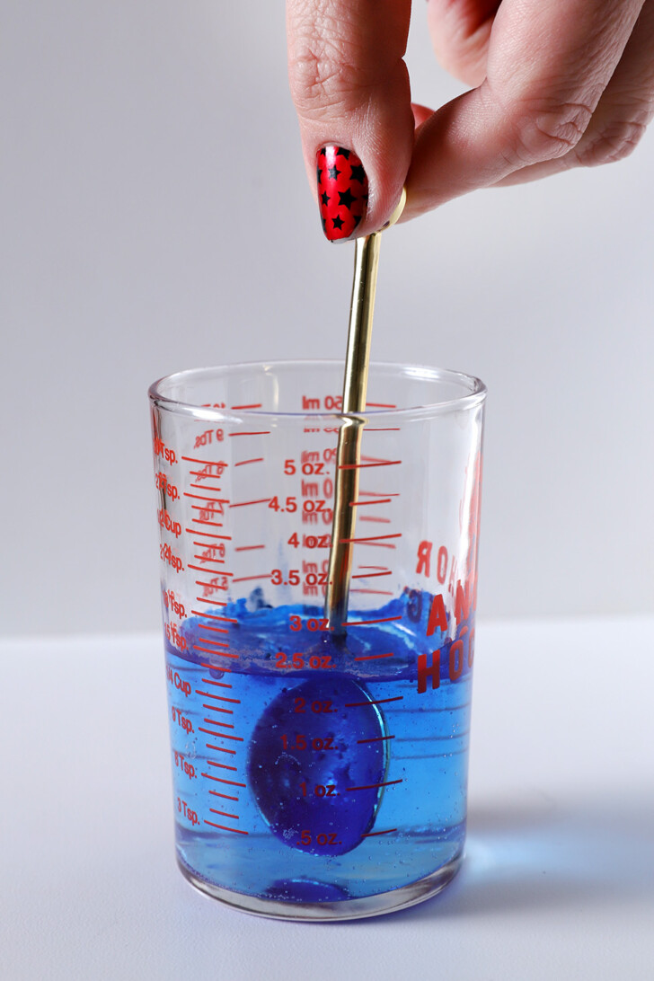 A hand stirring blue spirulina powder into water in a measuring glass.