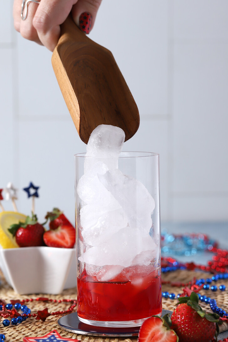 A hand pouring ice into a glass from a wooden scoop.