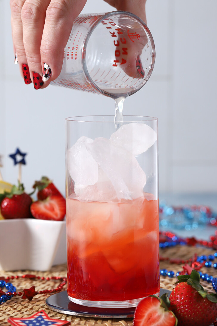 A hand pouring lemon juice from a measuring glass into a tall glass.
