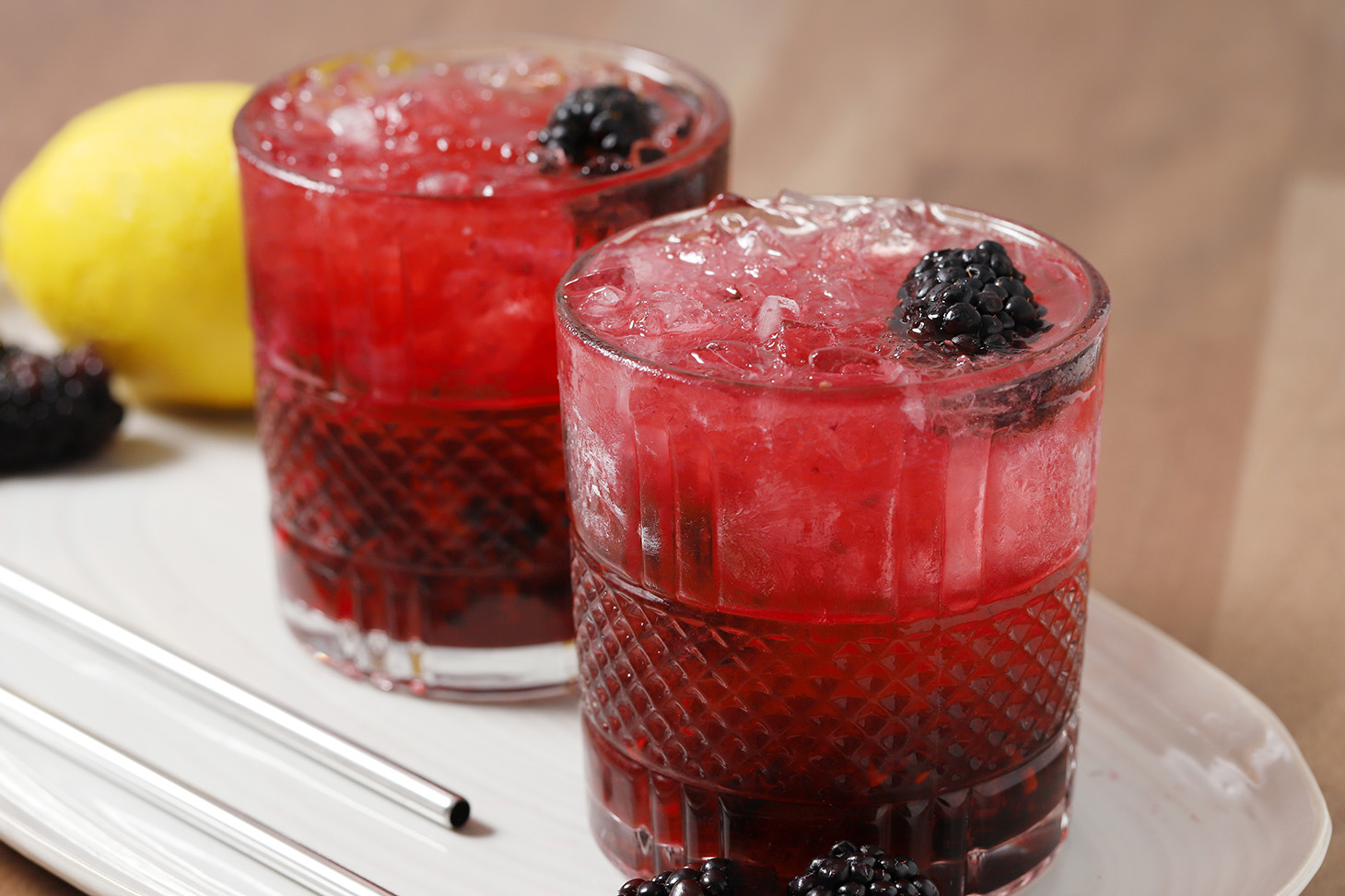 Two glasses of gin bramble on a tray garnished with blackberries.