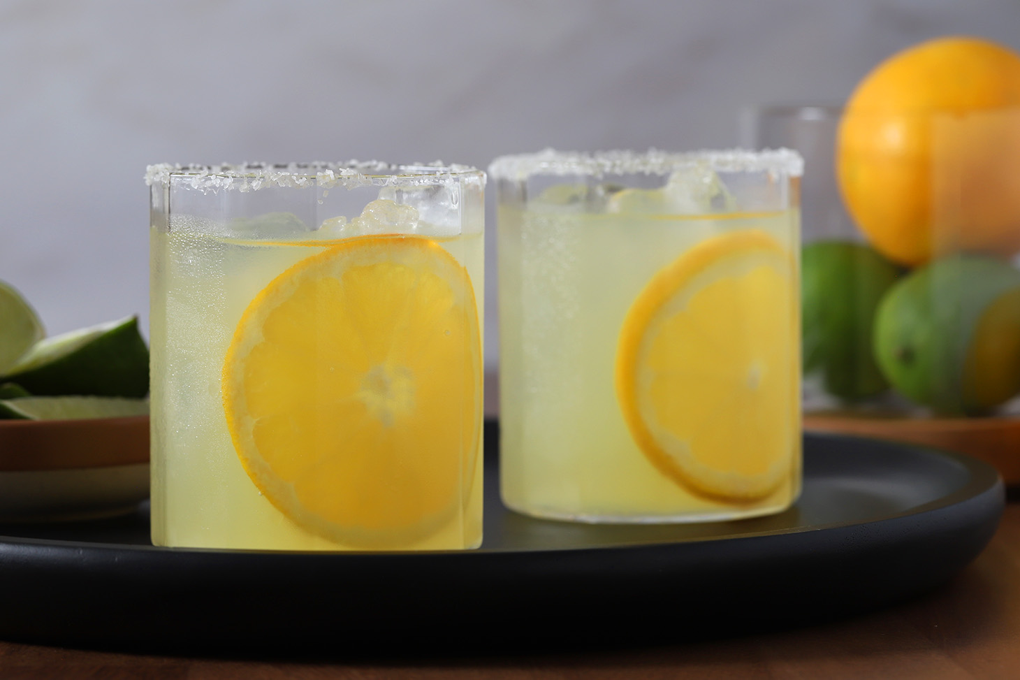 Two glasses of orange margaritas garnished with large orange wheels.