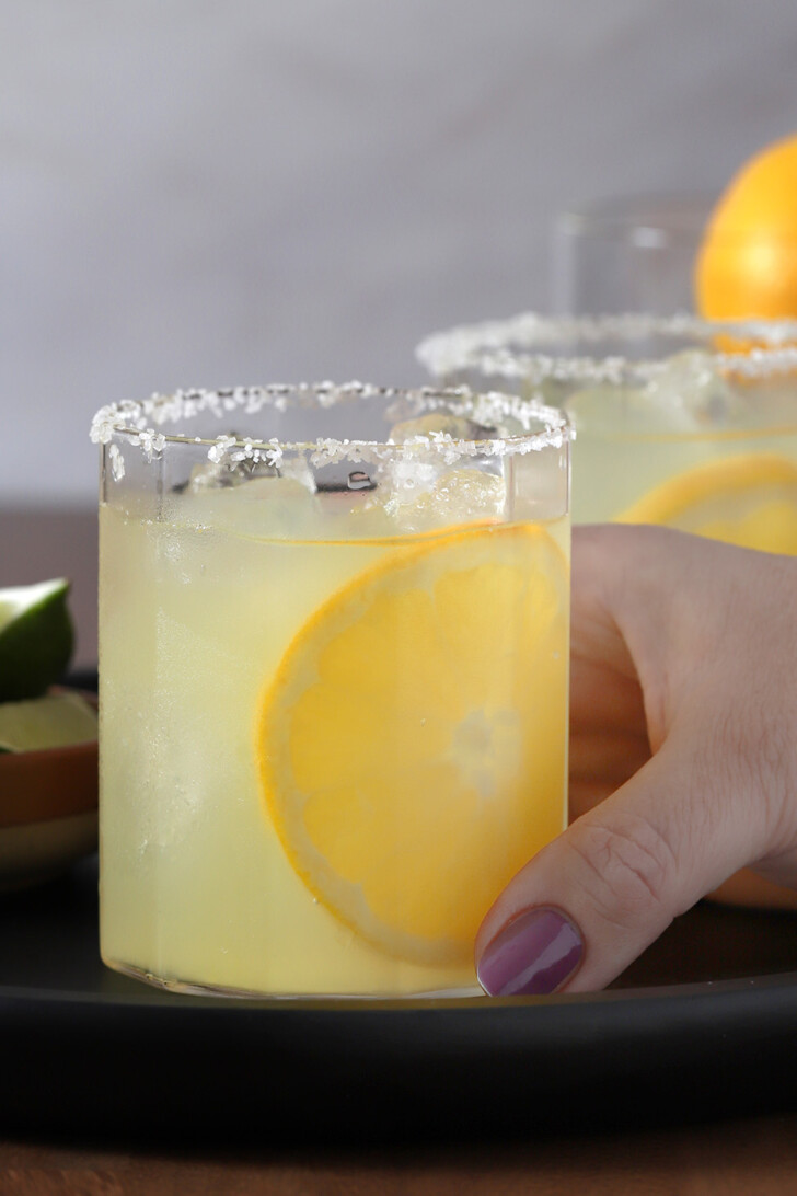 A hand reaching for a glass of orange margarita.