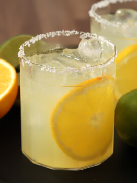 Glasses of orange margaritas garnished with salted rims and large slices of oranges.